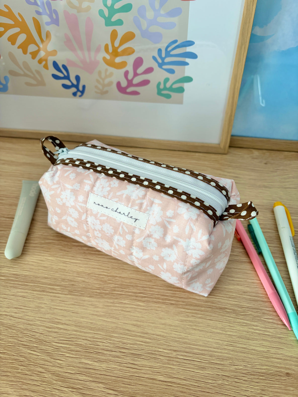 Floral colorblock bag with brown strap, front logo patch, pale pink floral fabric, zipper