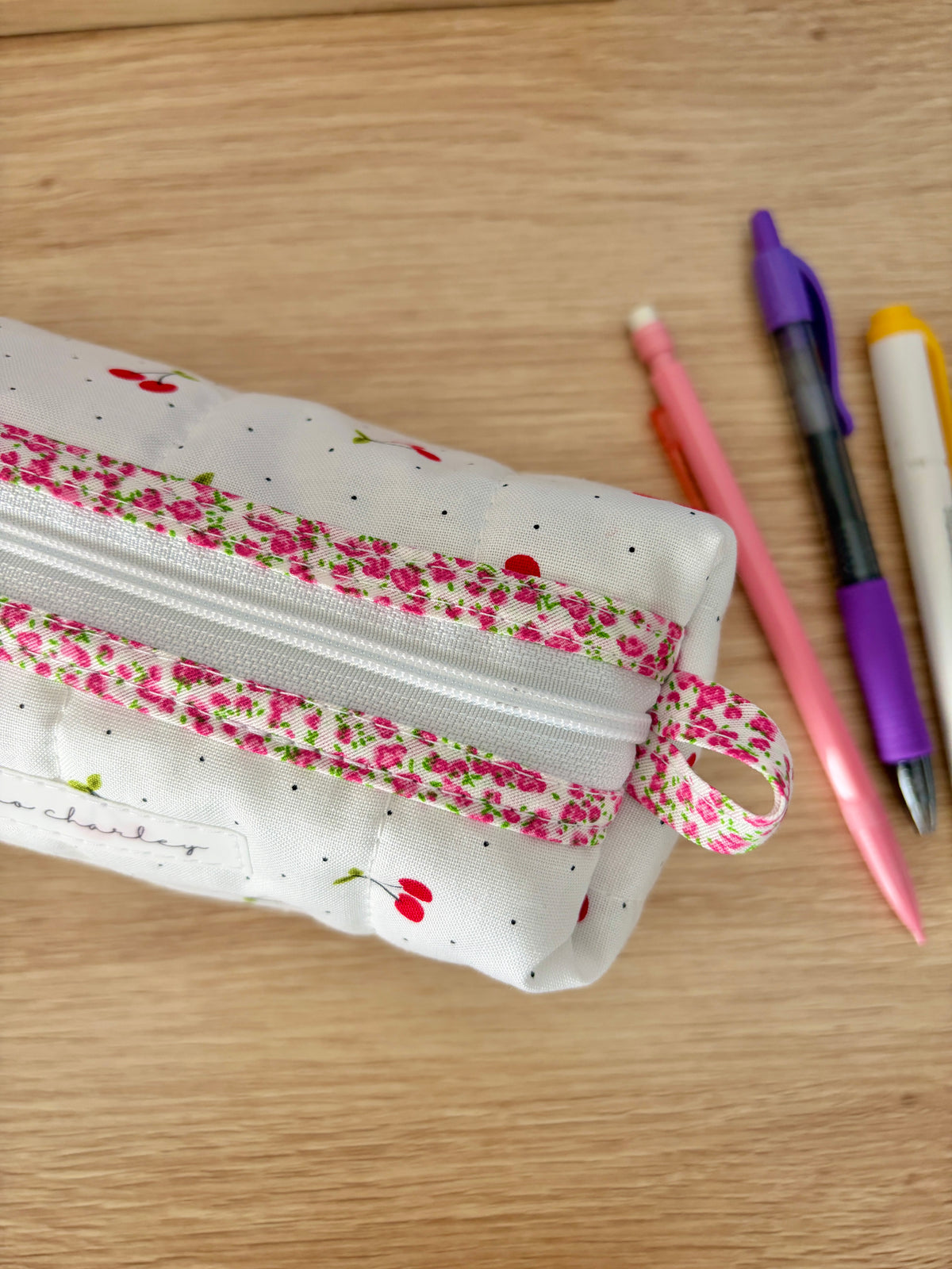 Cherry print zip pouch bag with pink-trimmed top and textured edge stitching; green lining