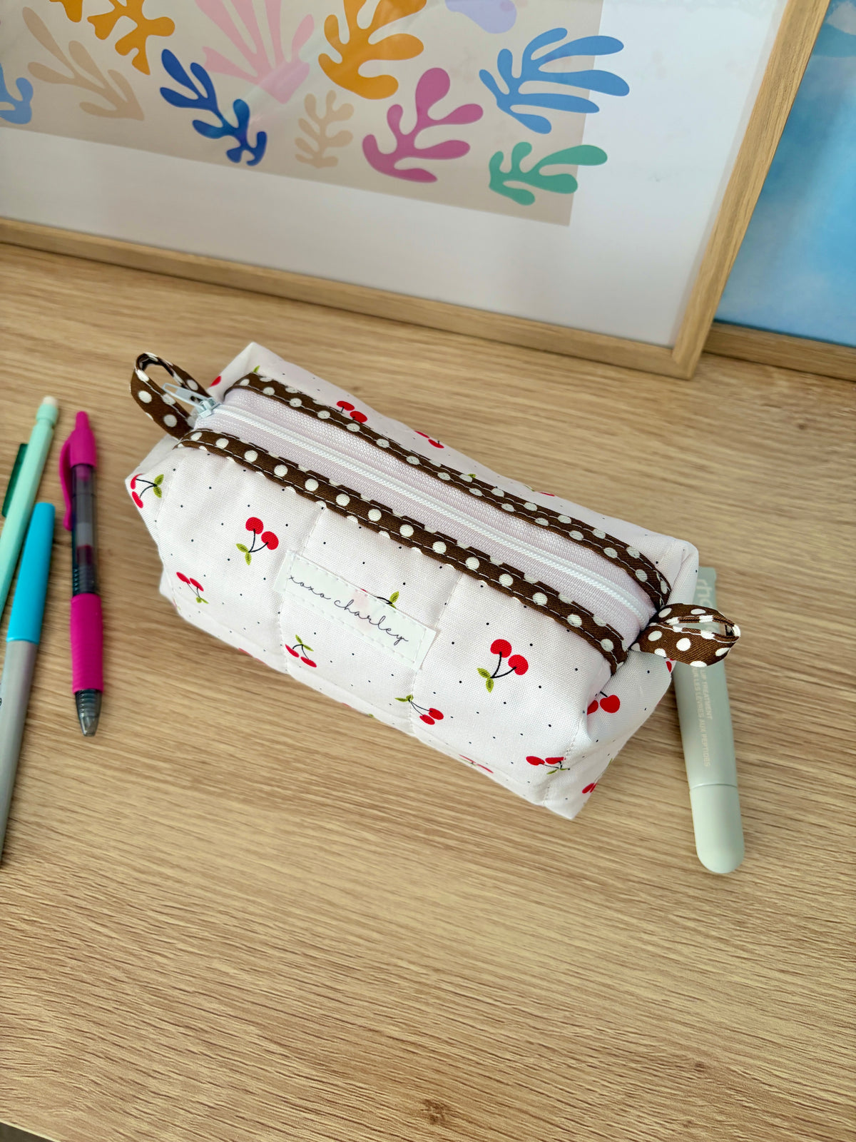 White fabric zip pouch bag with cherry print, brown trim, and side straps