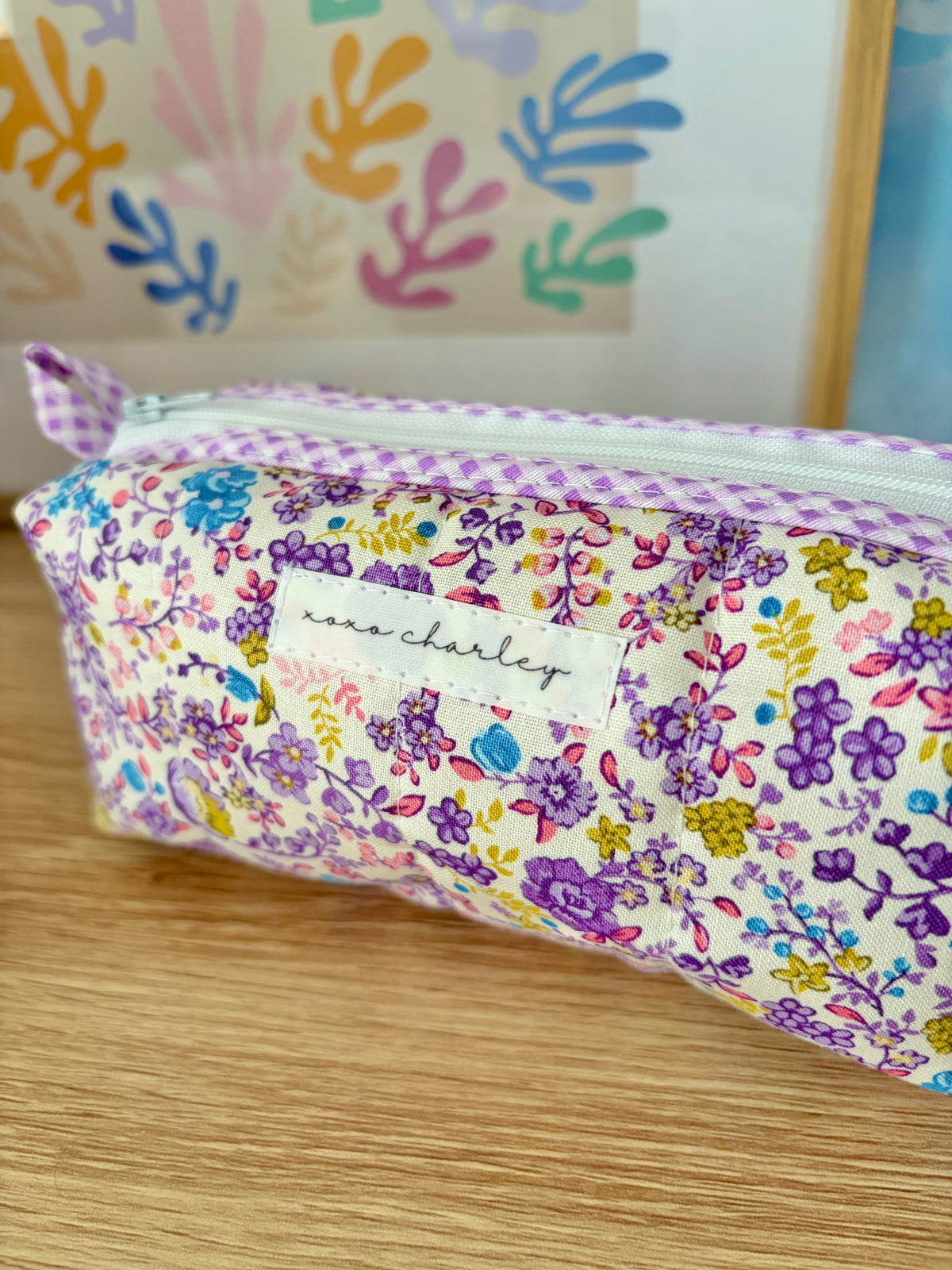Purple floral zipper pouch with stitched label reading "charley"