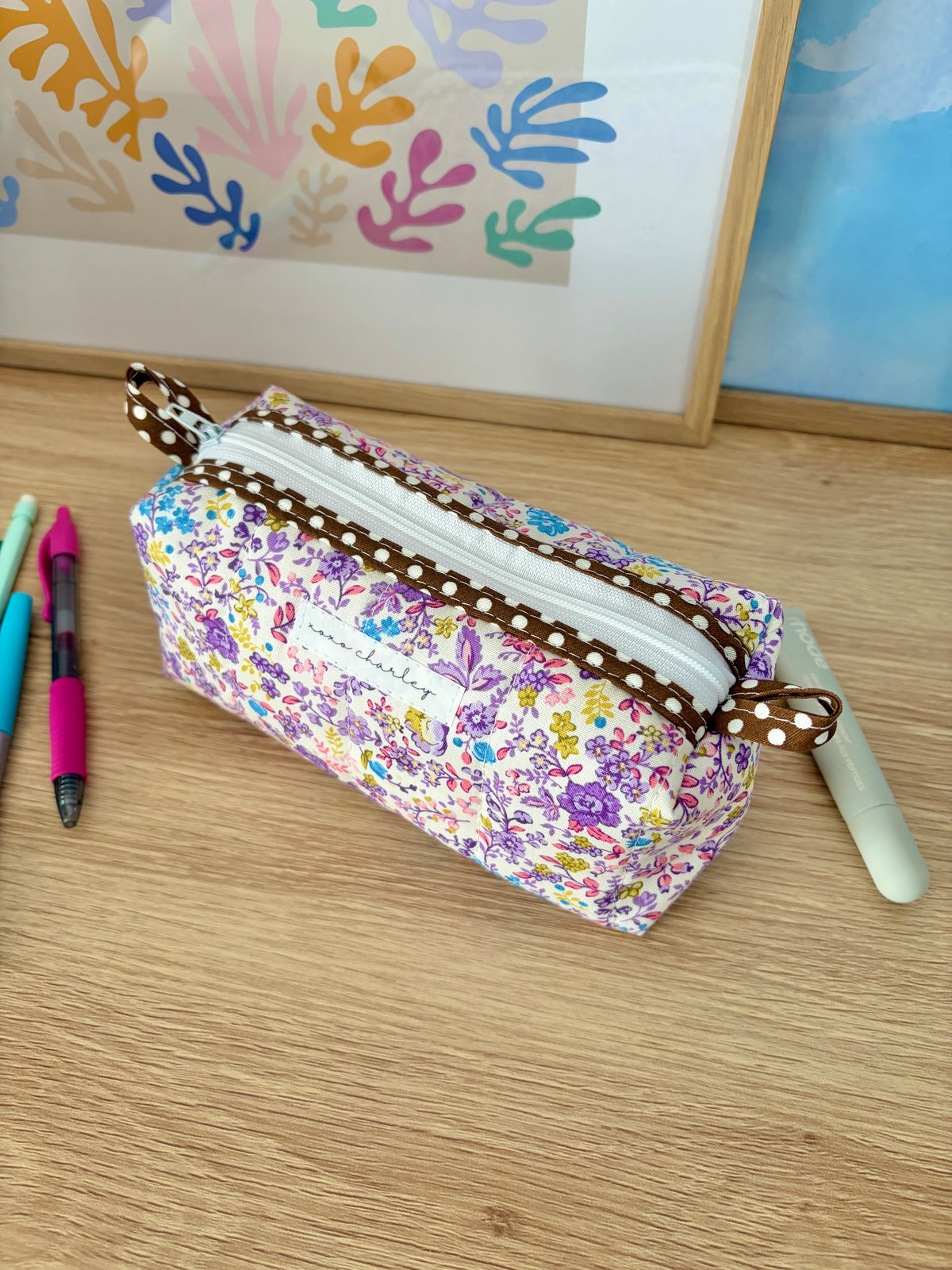 Purple floral zip pouch bag with brown stitched trim and loop strap