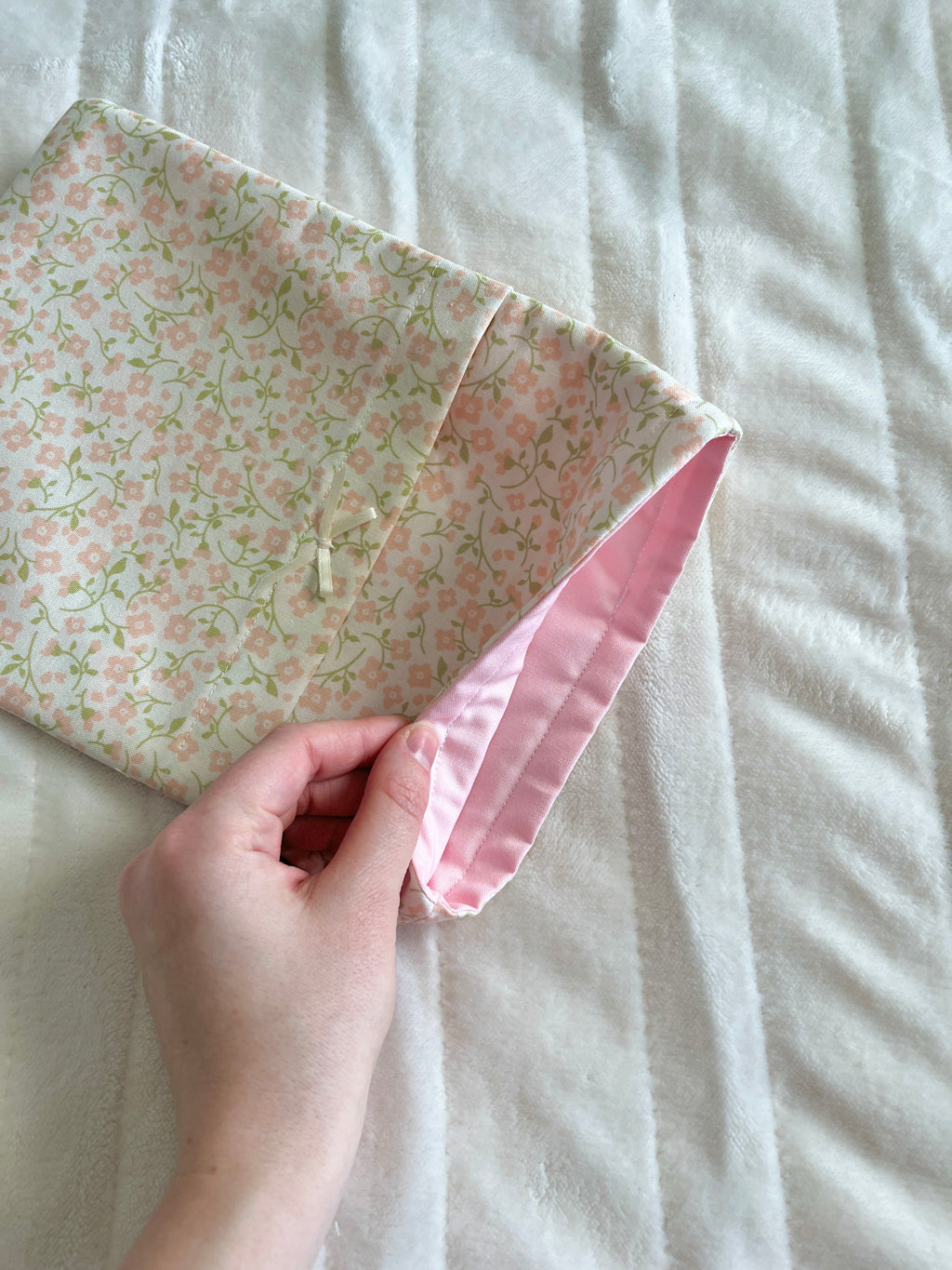Floral book sleeve with pink cuff and drawstring ties, held by hand