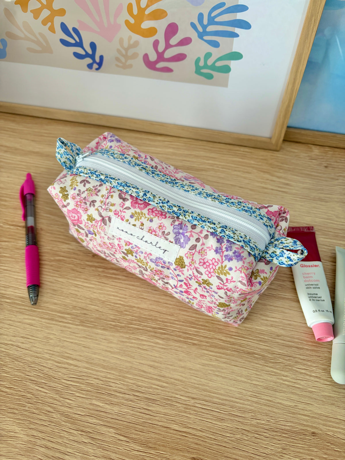 Zippered pencil pouch with pink floral exterior, blue trim, and patterned side panel.