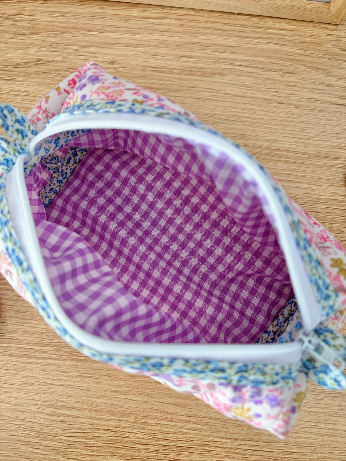 Close-up of open zippered pencil pouch with purple gingham interior and blue trim.