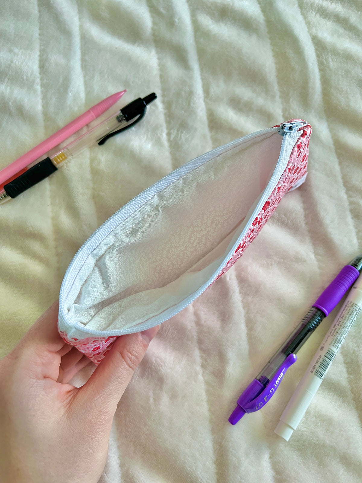 Pink floral zip pouch glasses case held open with pens and purple marker inside