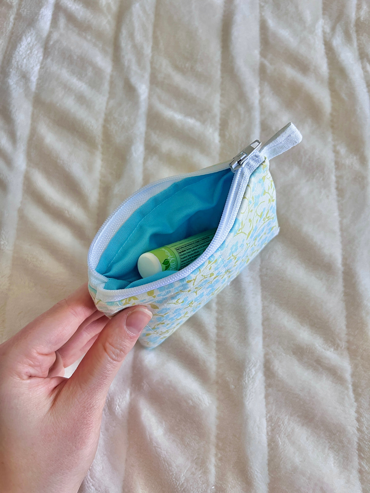 Light blue floral zipper pouch wallet with blue lining, opened to reveal contents