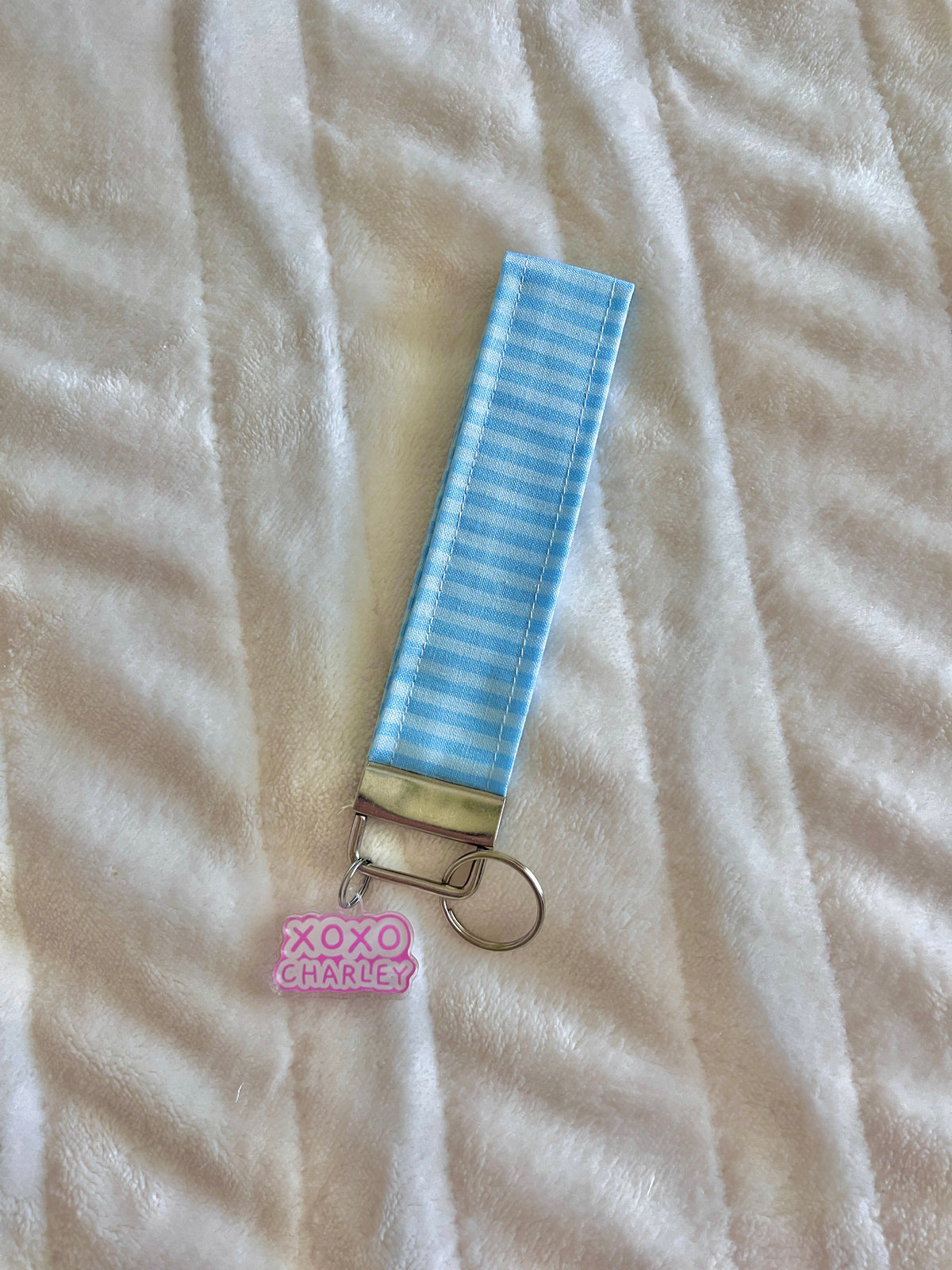 Blue striped wristlet keychain with metal clasp and pink XOXO CHARLES tag