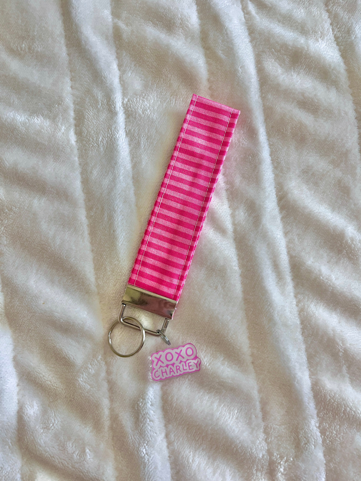 Pink striped keychain wristlet strap with metal clasp and small logo charm