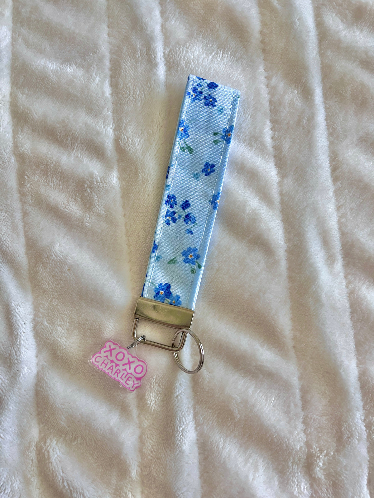 Floral keychain wristlet with light blue ribbon strap, metal ring, and pink charm