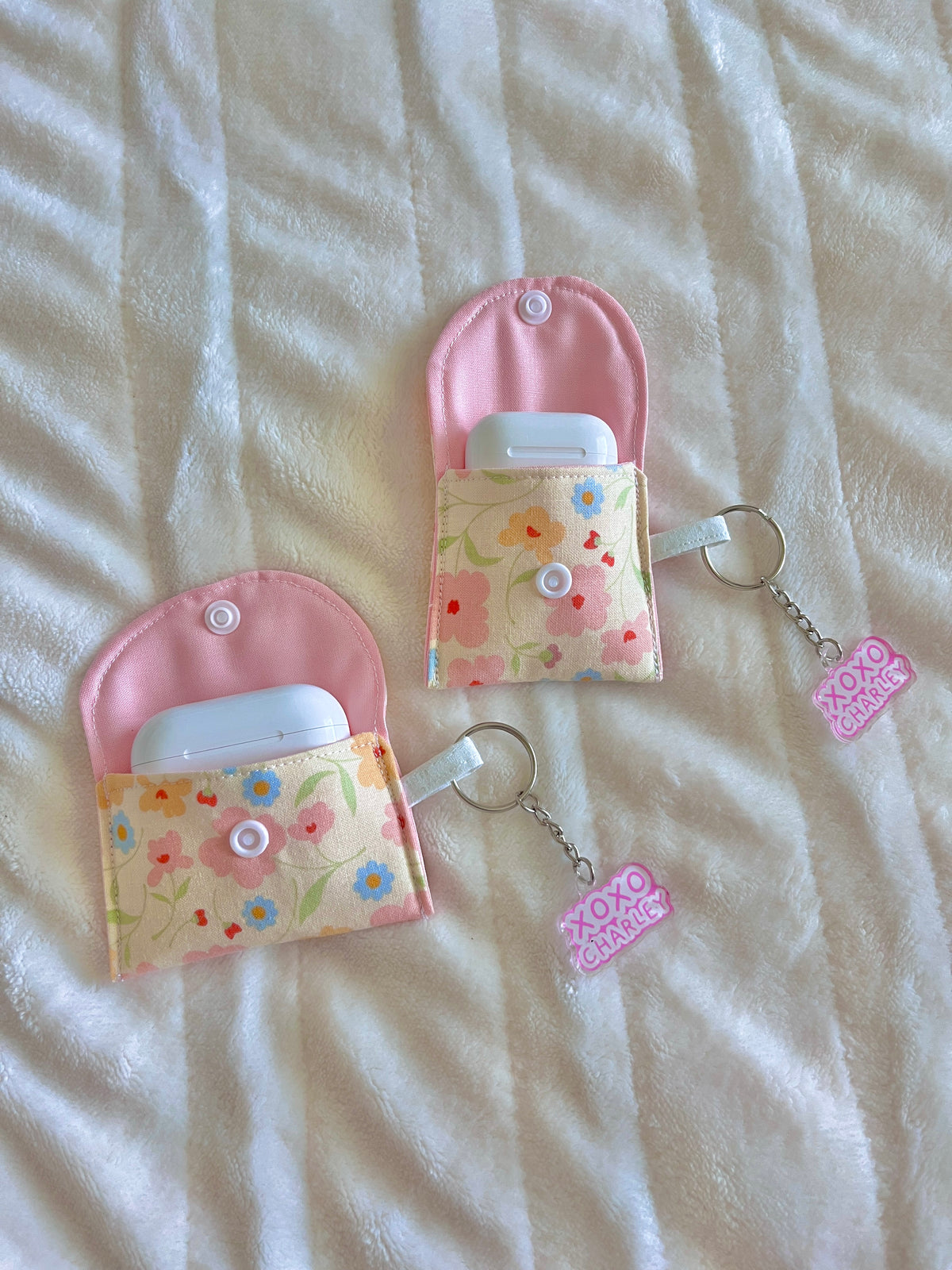 Pink half-moon earbud case pouch with floral flap and keyring, with two tags