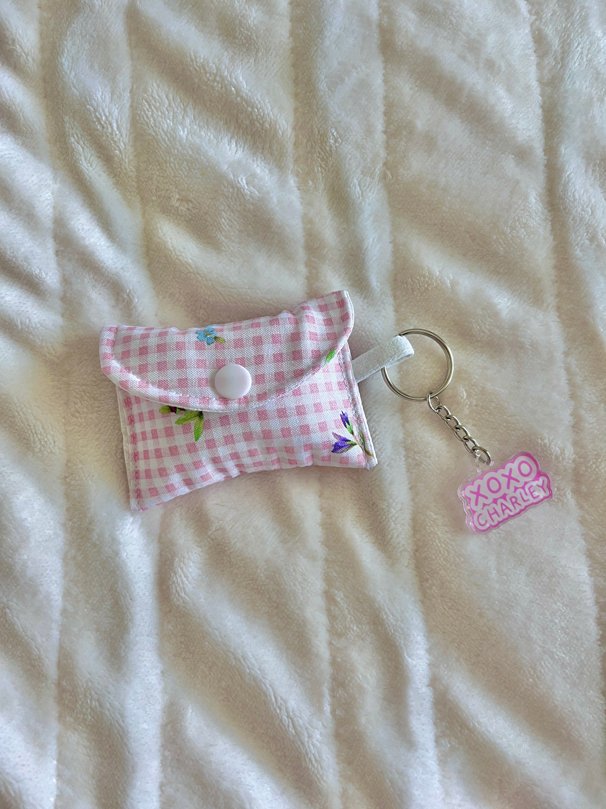 Pink gingham earbuds case with small flower patch and round snap button, keychain charm.