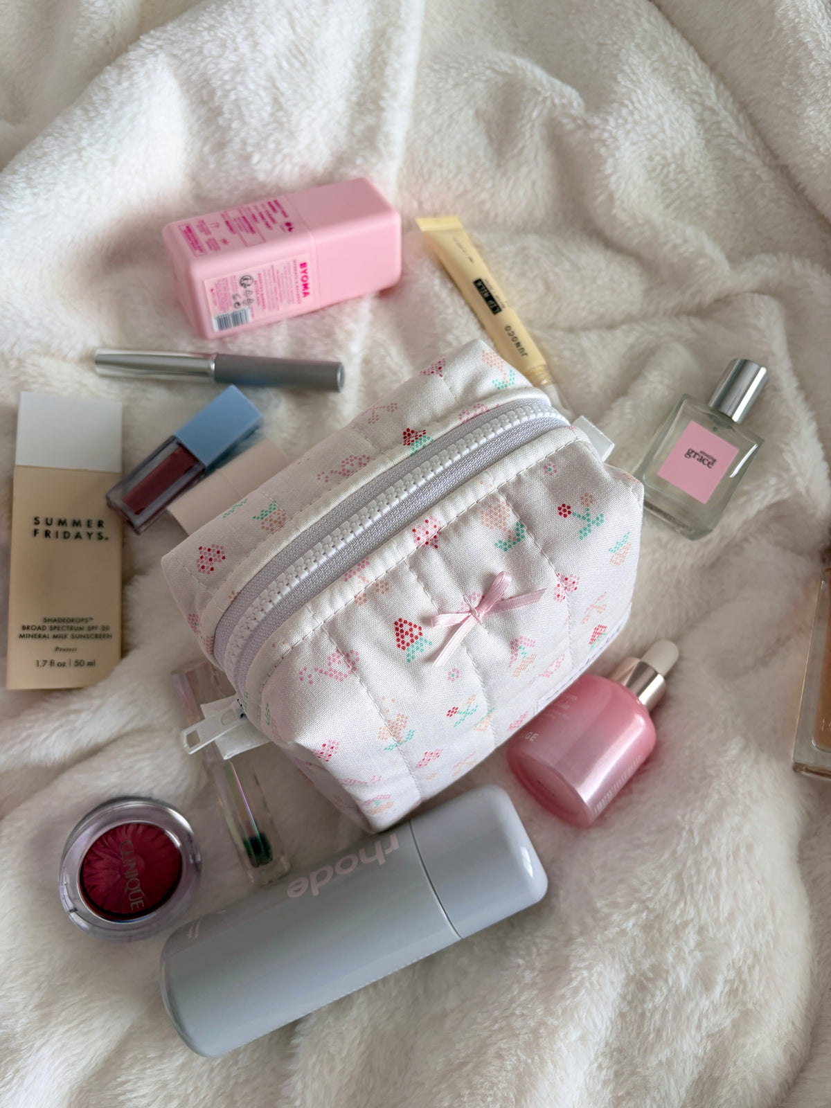 Mini makeup bag with light-colored bow, patterned white fabric, top zipper pocket