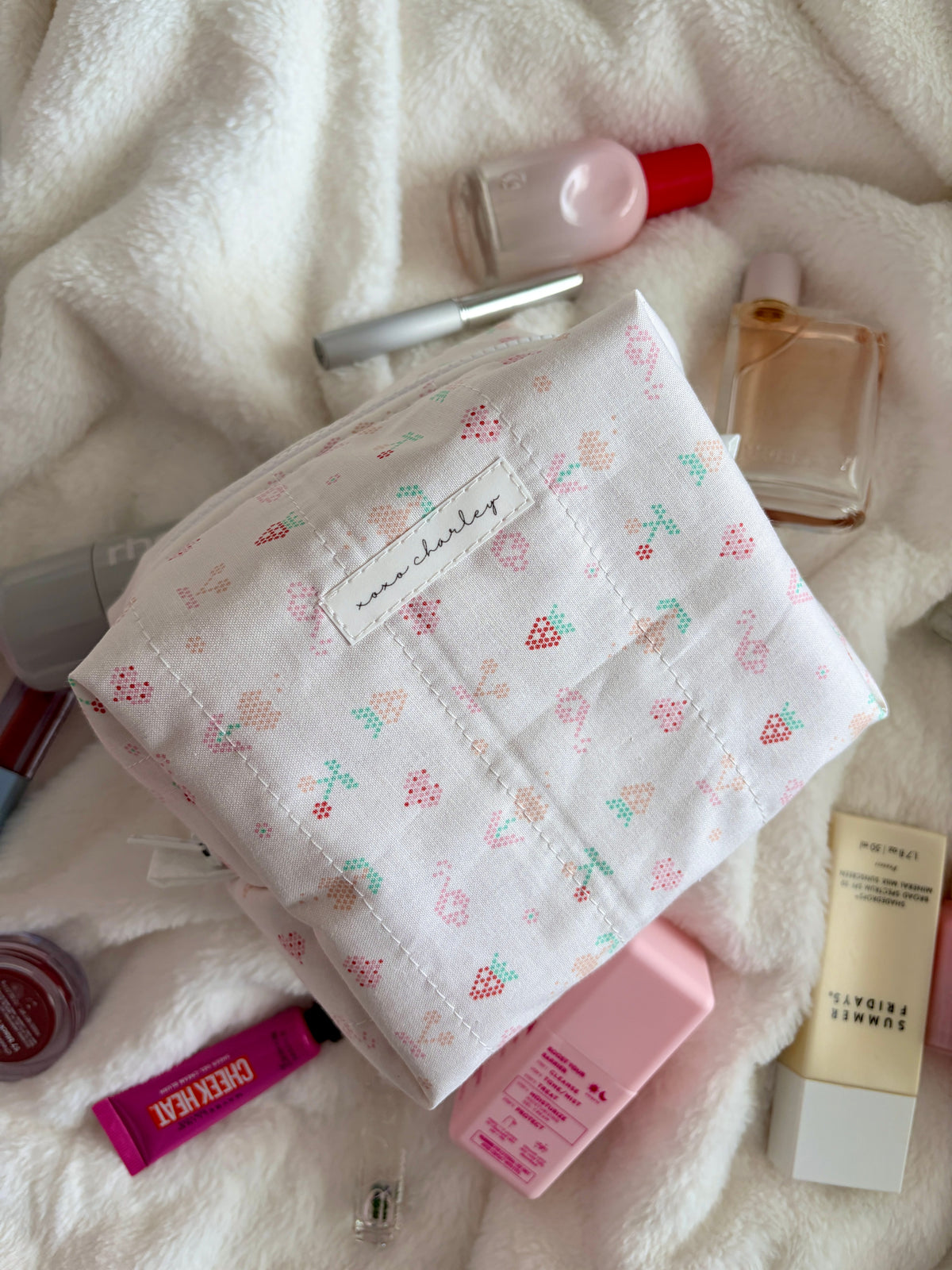 Medium makeup bag, white with small multicolor icons; visible zipper pocket and red gingham interior.