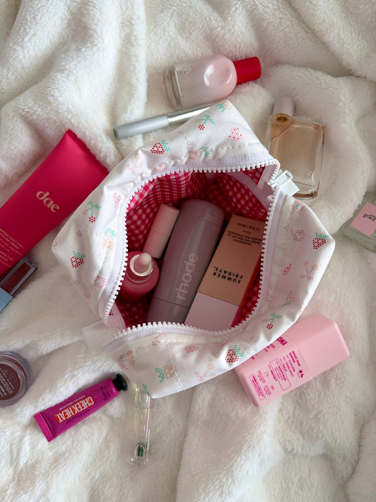 Medium makeup bag with white fabric and colorful icon pattern; open top reveals red gingham lining.