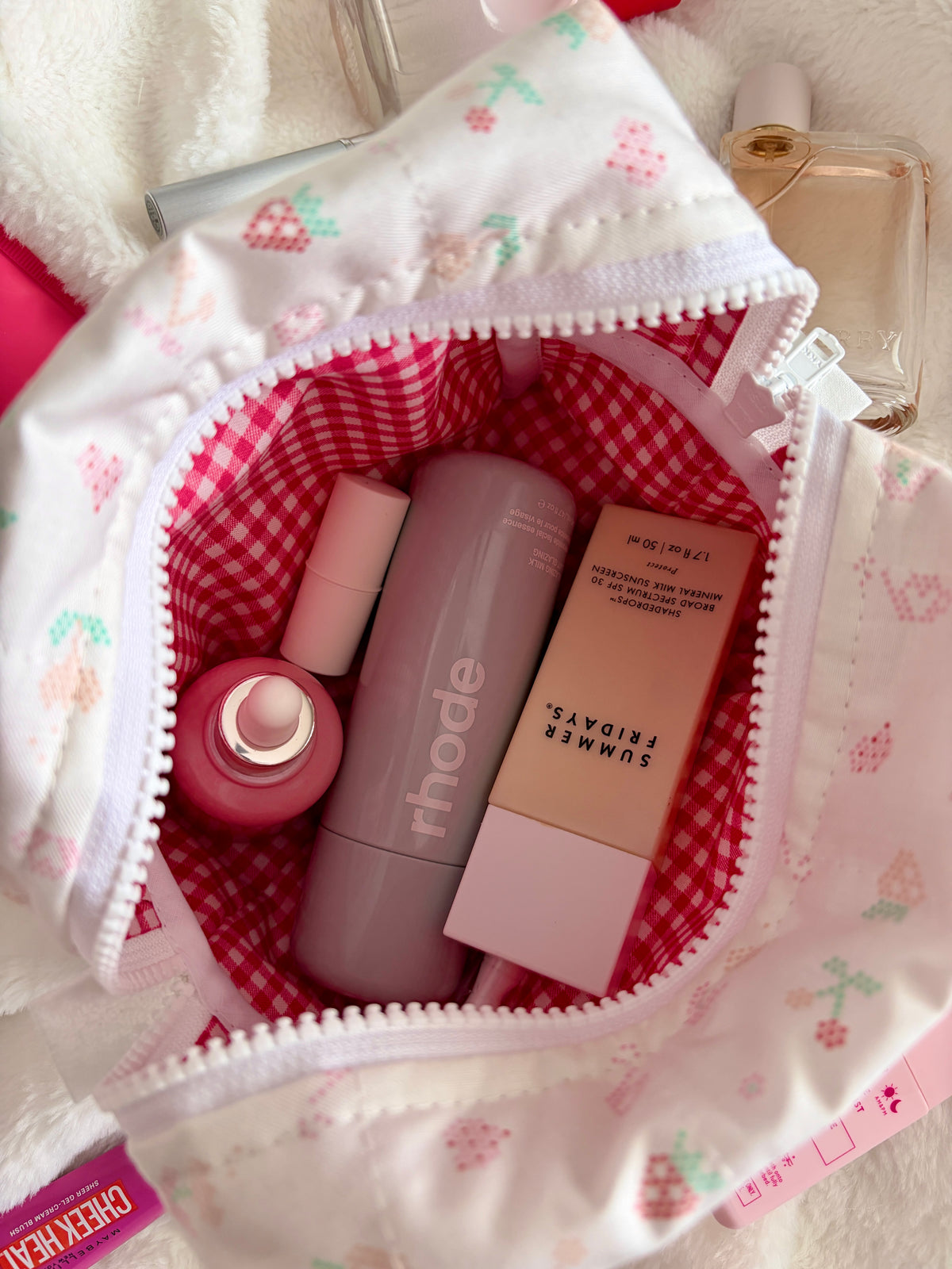 Medium makeup bag open wide, showing red gingham lining and assorted lip and skincare bottles.