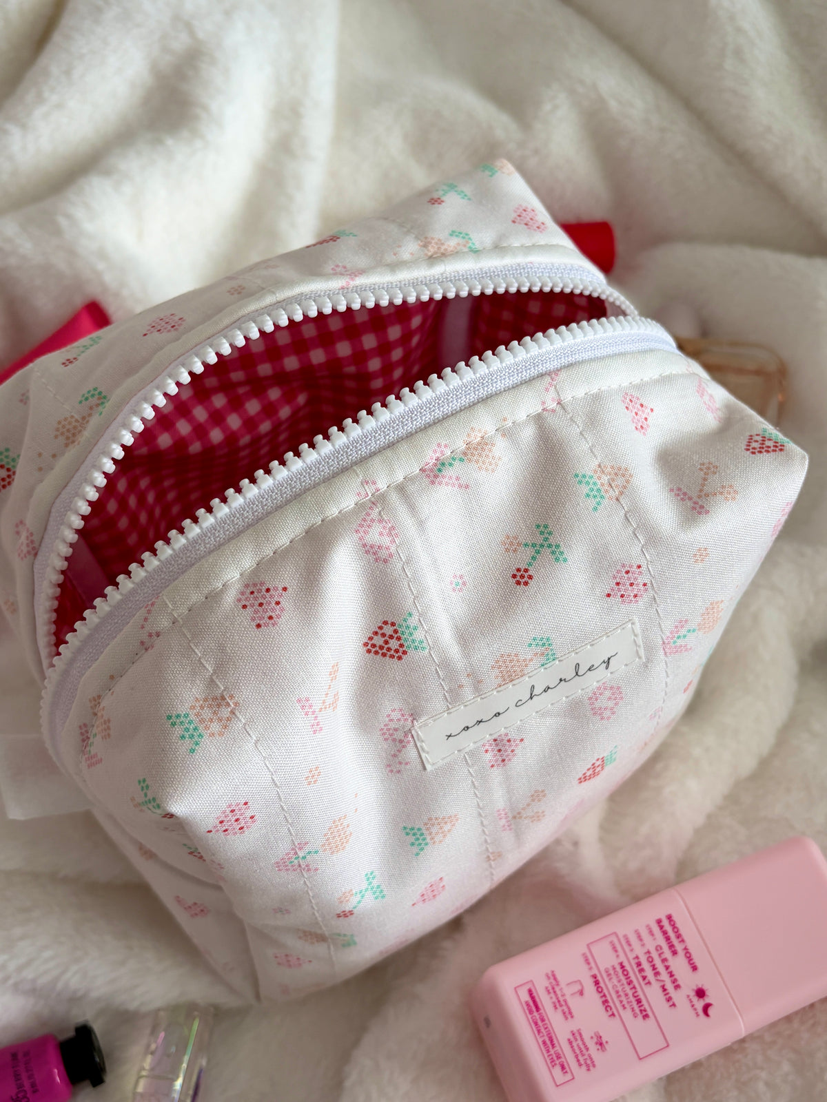 Medium makeup bag angled view, red gingham lining peeking from white patterned zipper top.