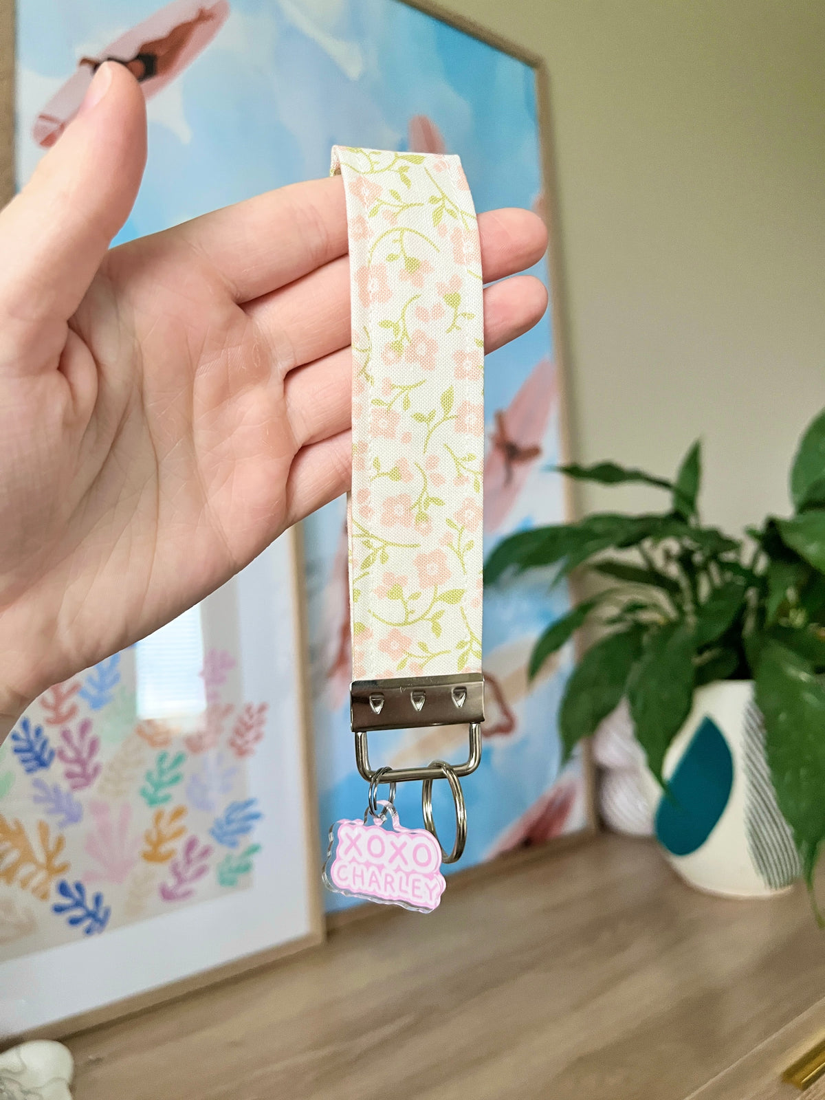 Floral keychain wristlet with gold snap clasp and XOXO Charley tag, held in hand