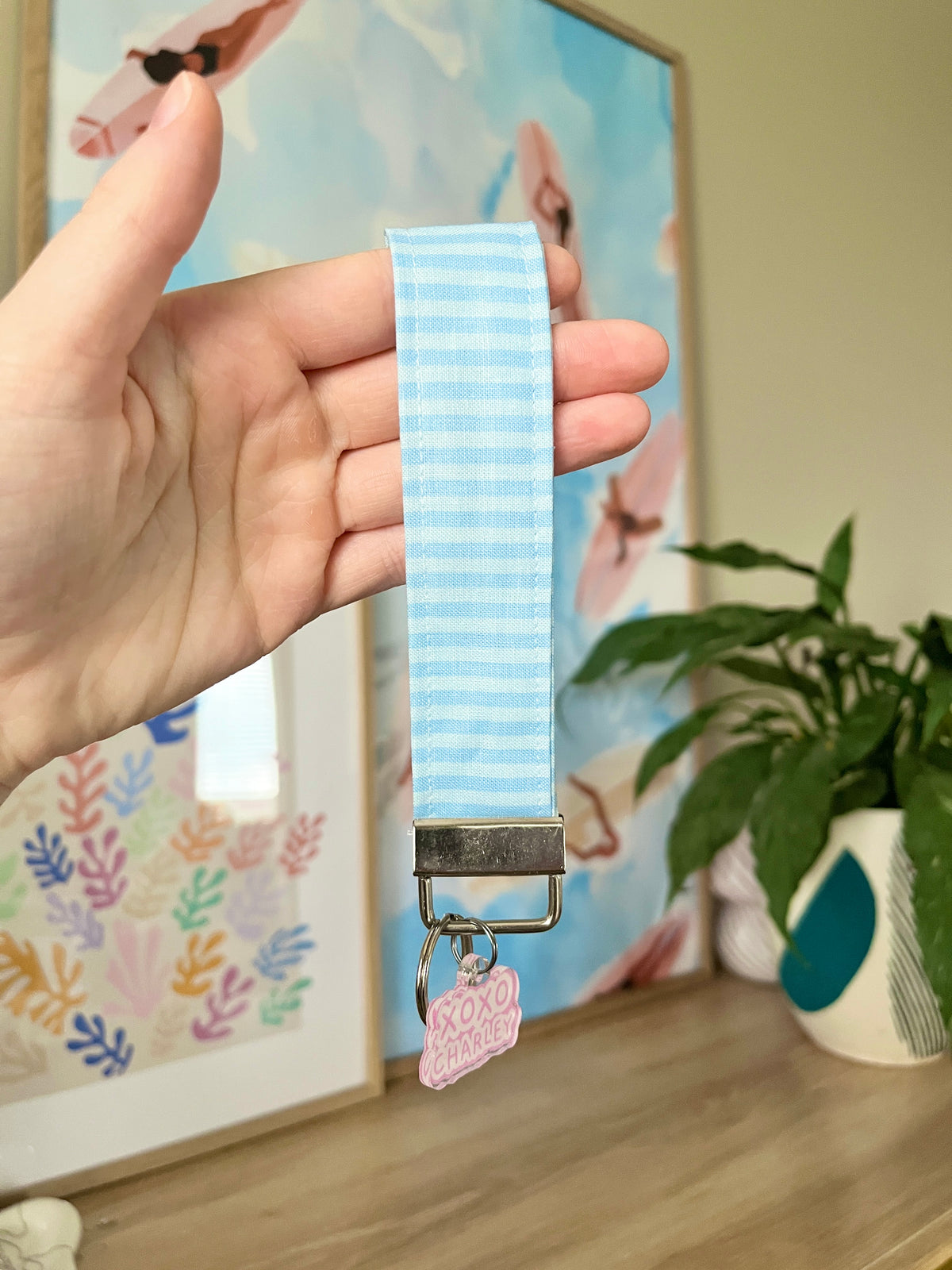 Blue striped wristlet keychain held in hand with metal clasp and XOXO CHARLES tag
