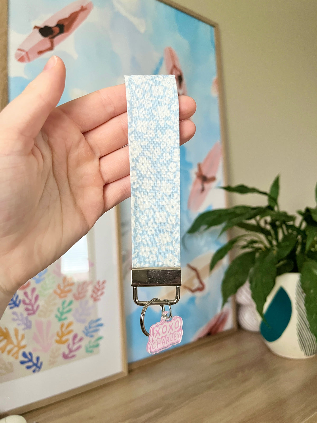 Blue floral wristlet key strap with silver clasp and pink XOXO charm, held