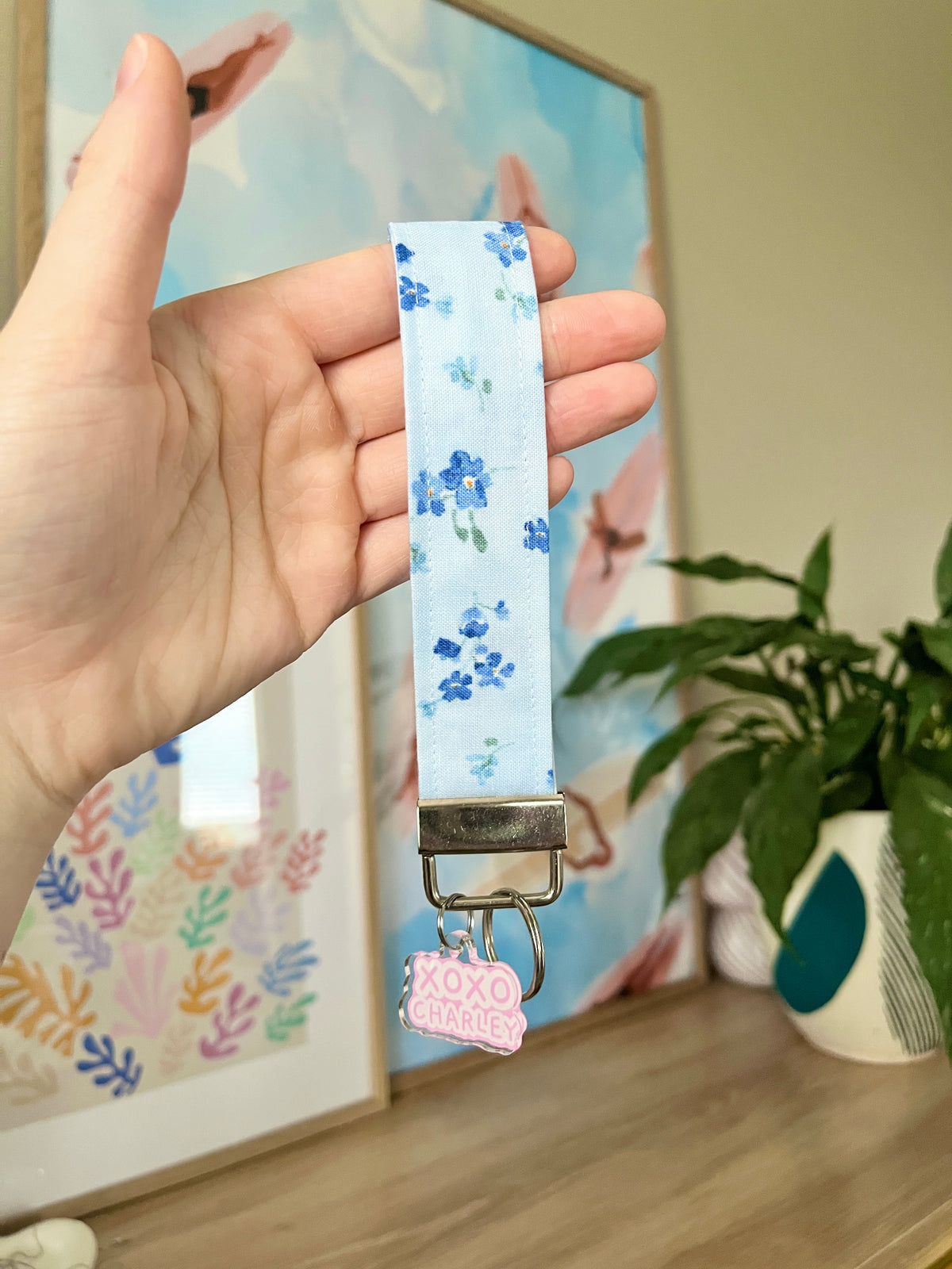 Floral keychain wristlet ribbon strap with clasp and pink XOXO charm, held in hand