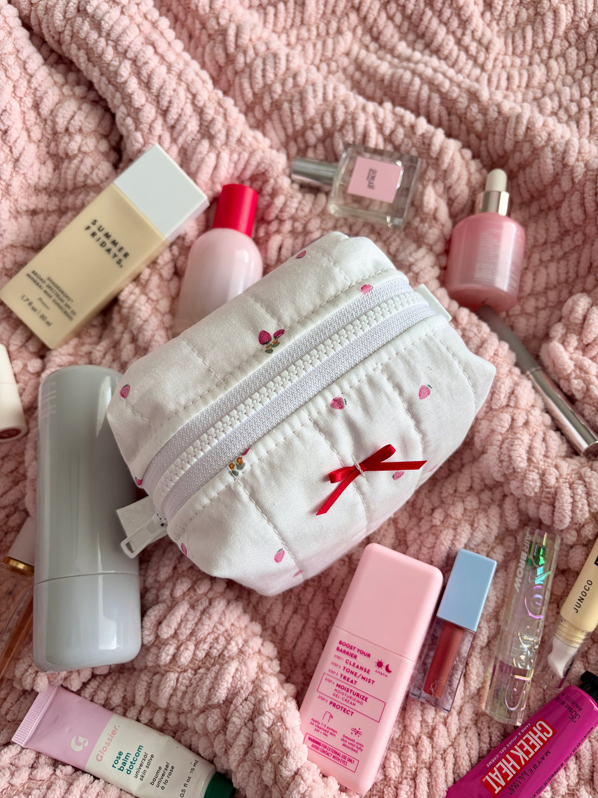 White mini makeup bag with red ribbon bow, embroidered motifs, and zip closure