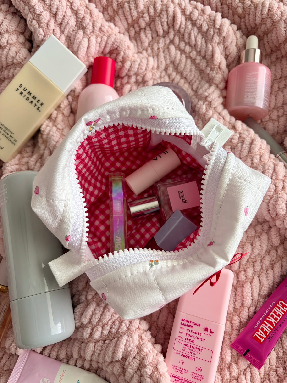 White mini makeup bag open with red gingham lining showing makeup bottles and tubes