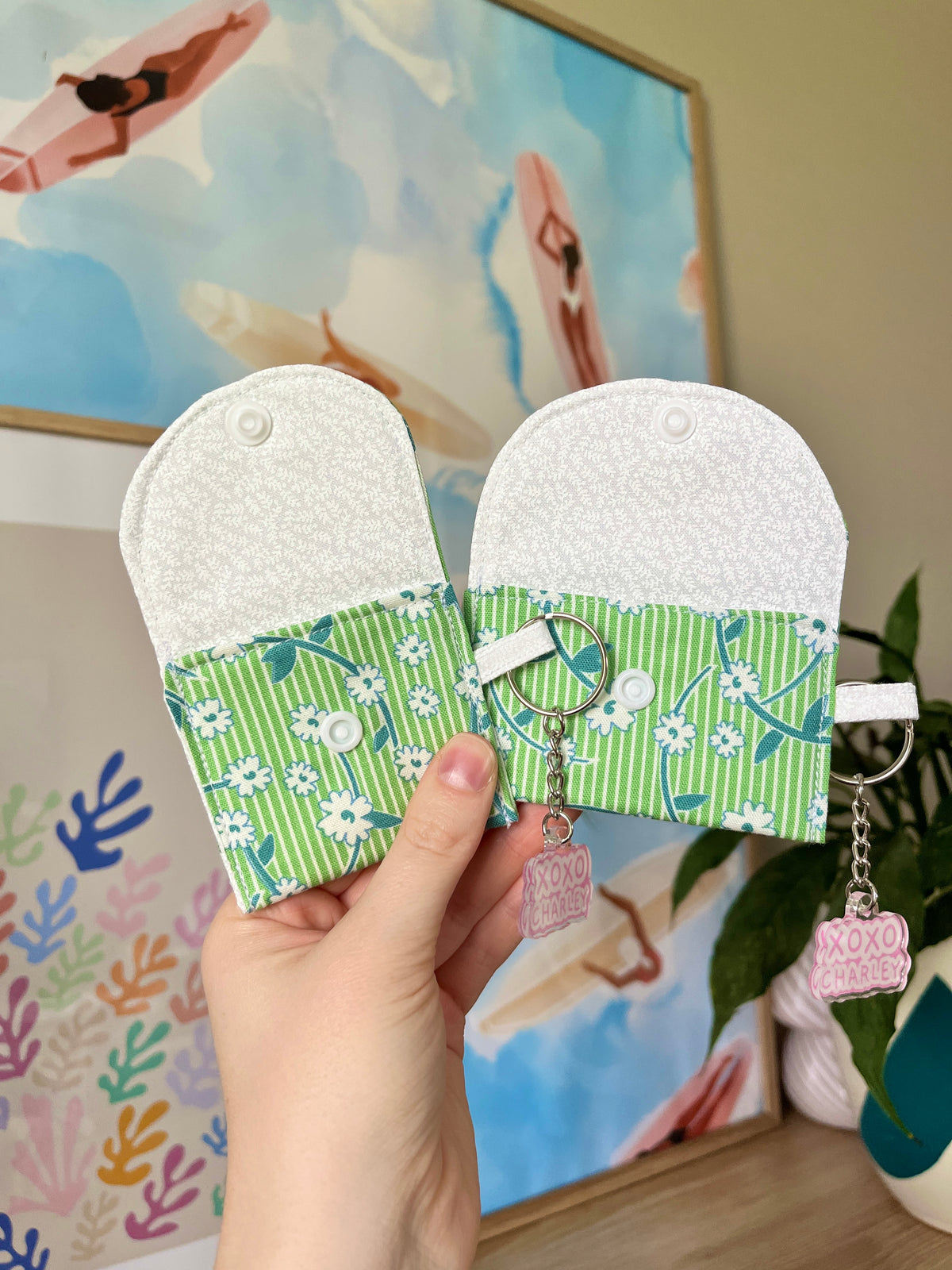 Green floral earbud cases with snap closure and keychain rings, held in hand