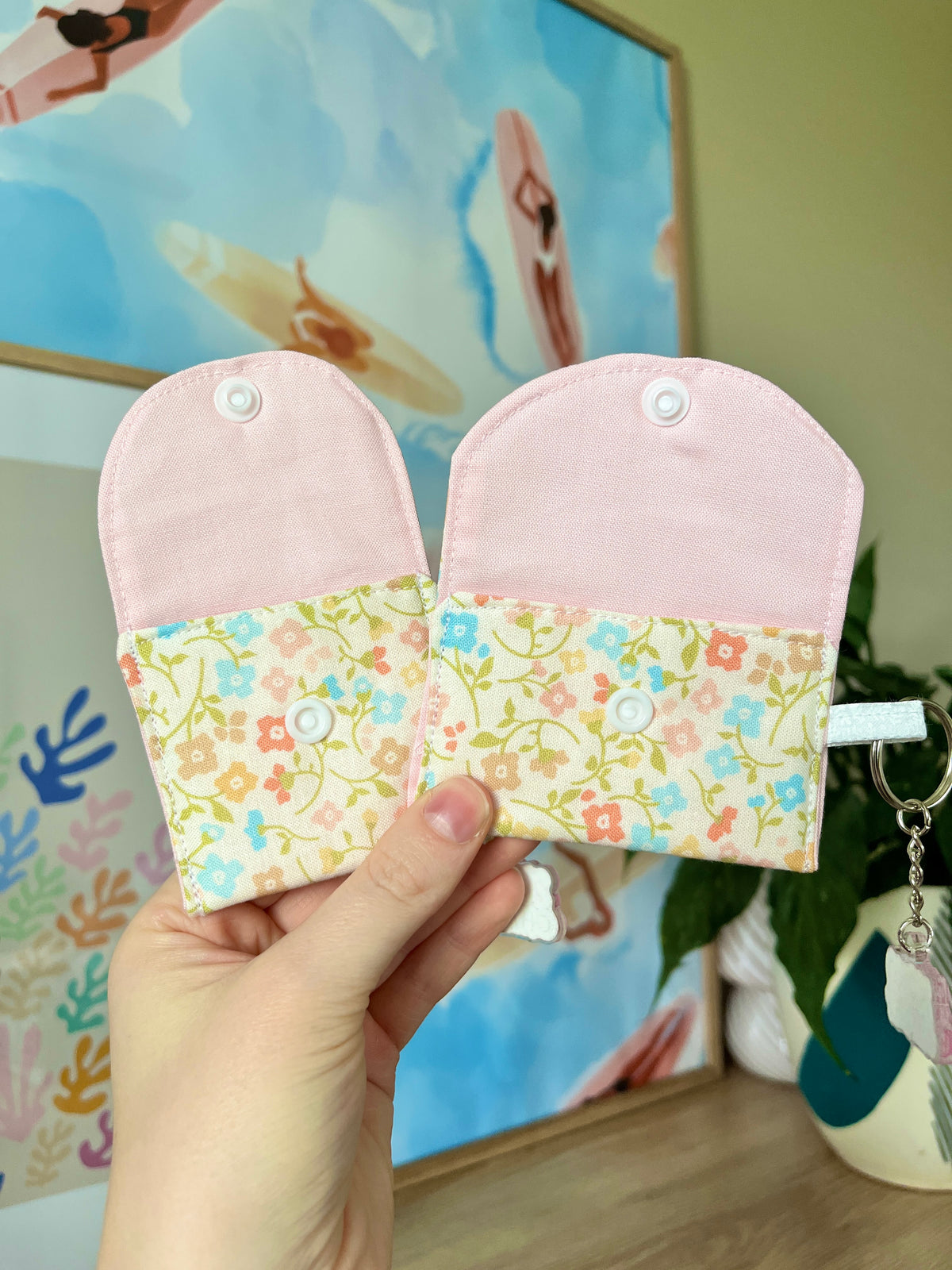Pair of pastel earbud cases with pink tops, floral panels, and snap keyrings