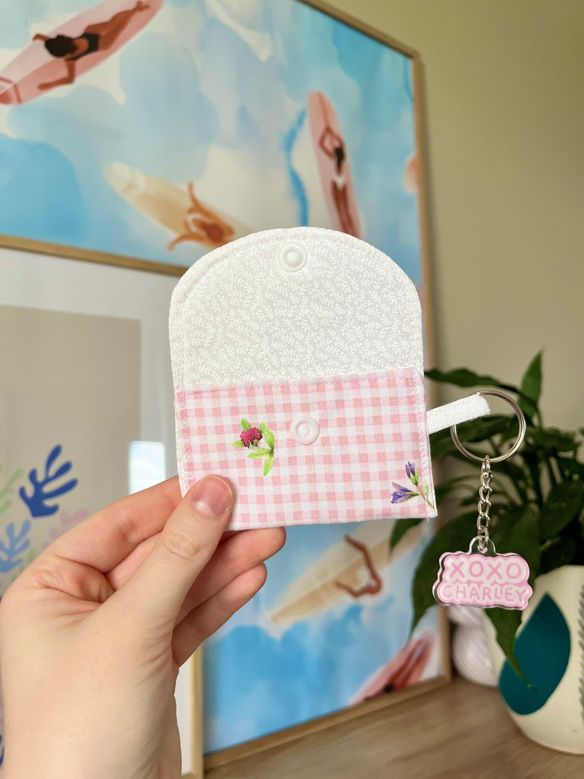 White sherpa-style earbuds case with pink gingham front panel and keychain charm.