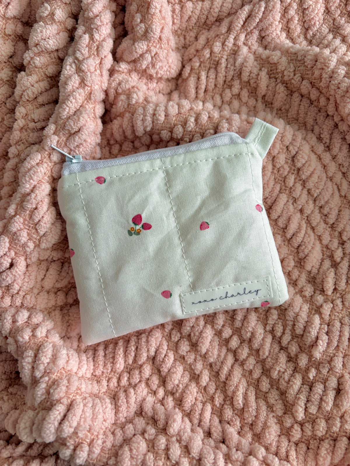 Small light-colored pouch with floral embroidery on a pink textured fabric background