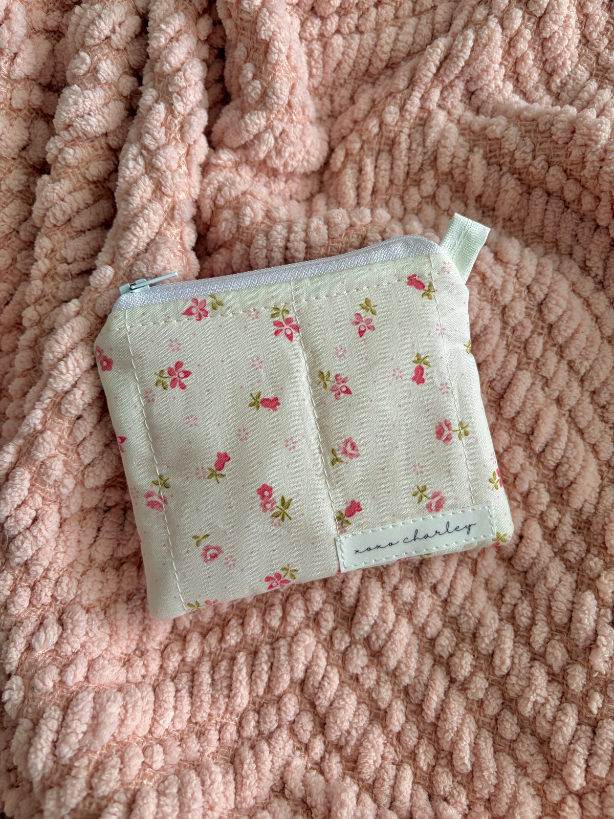 Small floral-patterned pouch on a pink textured fabric background