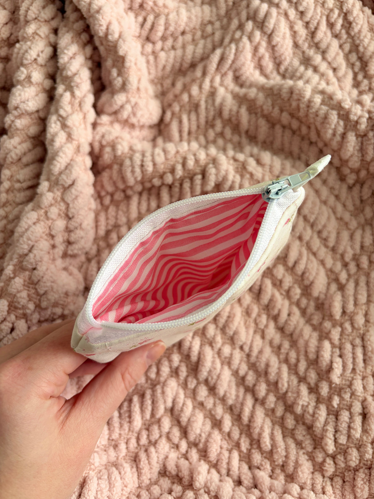 Hand holding a small pouch with a pink interior against a textured pink background