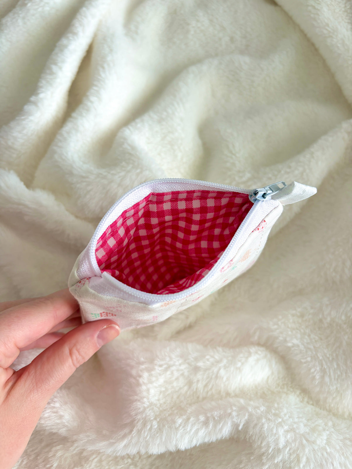 Small pouch with a red checkered interior held against a white blanket.
