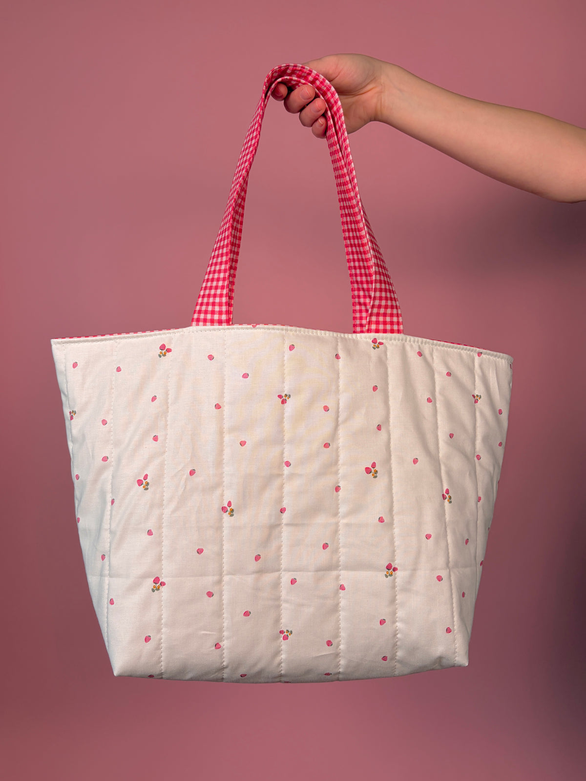 Large tote bag held by red gingham top handles; white fabric with berry flower pattern