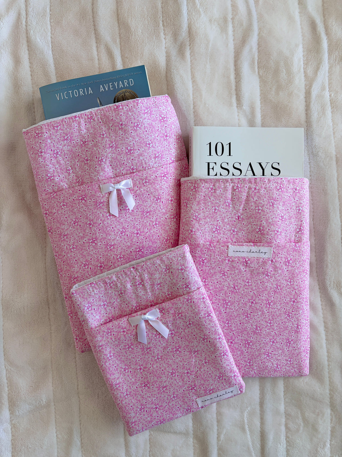 Pink floral e-reader and book sleeves with ribbon bows, stacked with a matching cover