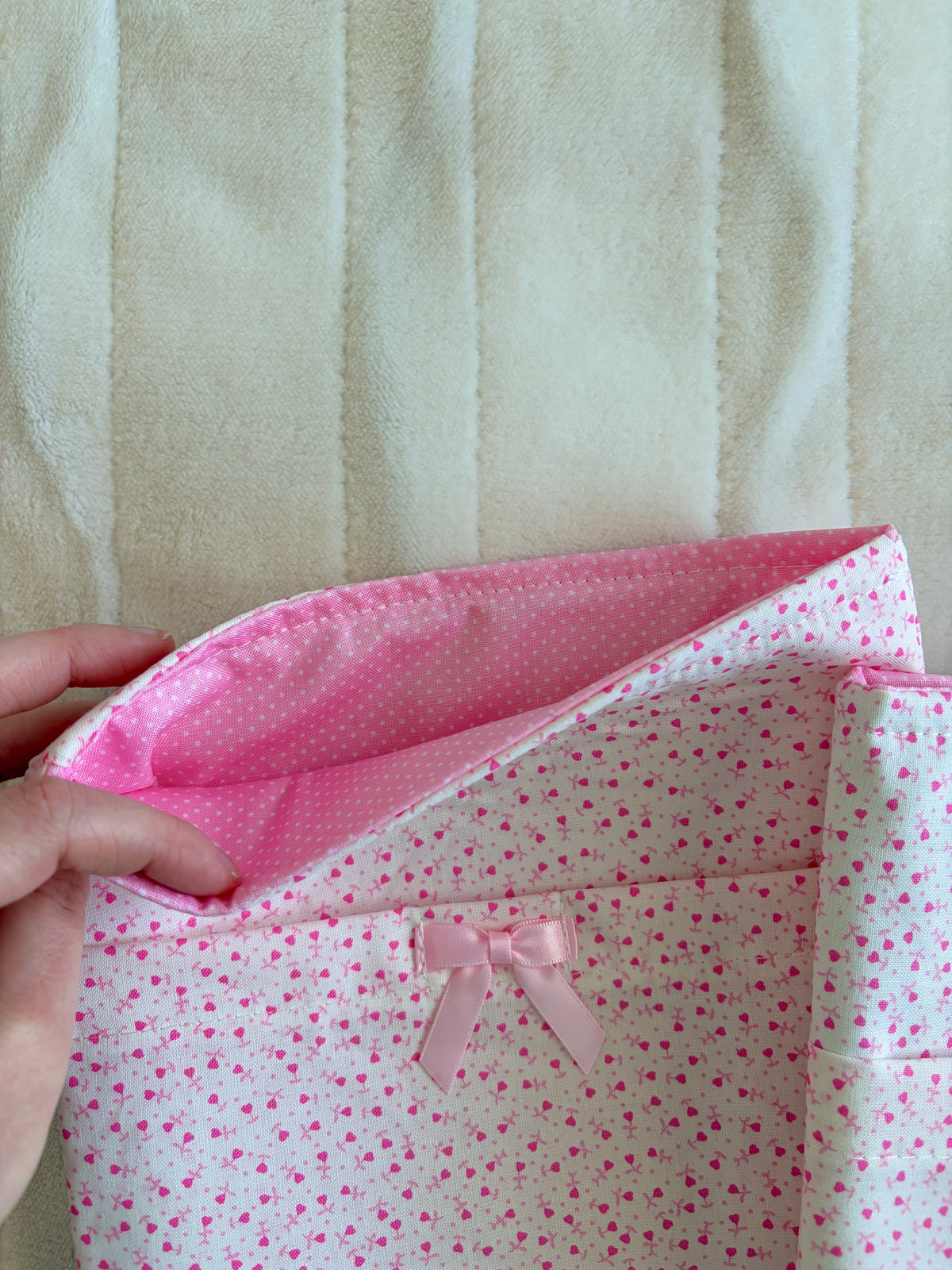 Pink heart-pattern sleeve with flap and satin bow, side view held in hand