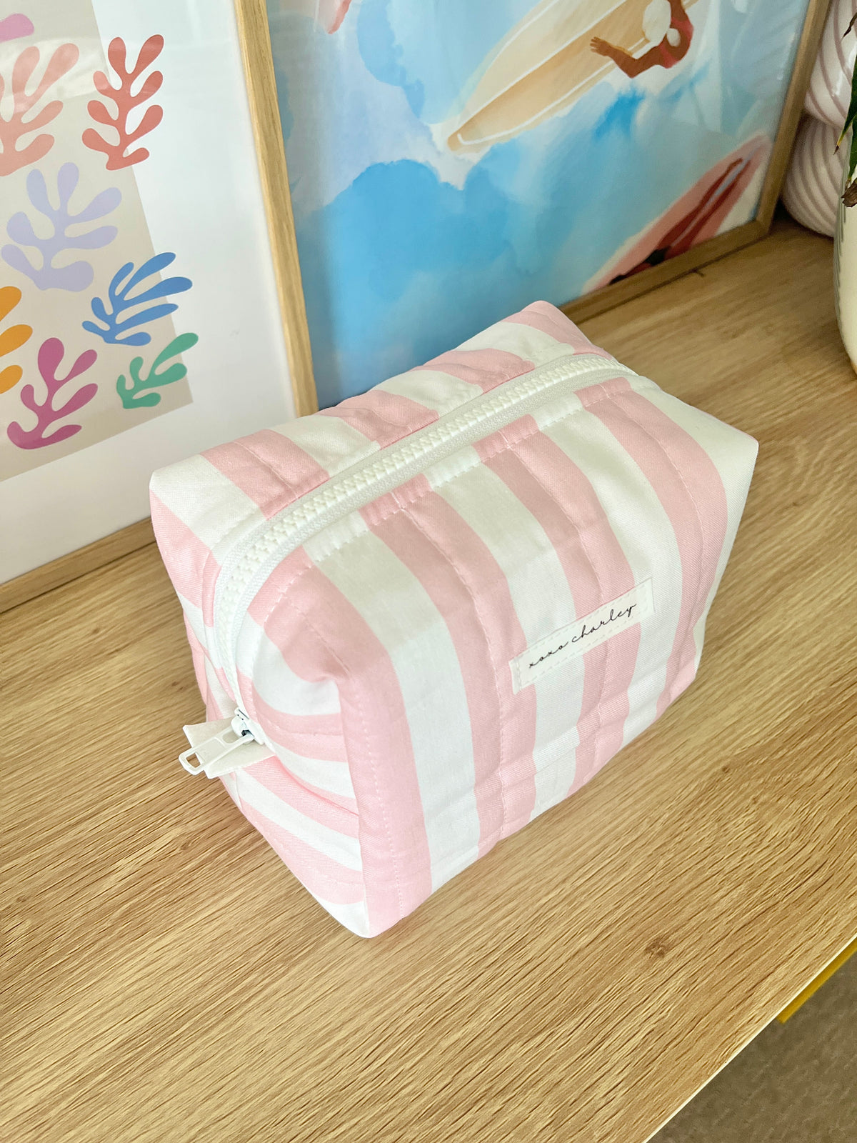 Pink and white striped medium makeup bag, angled view with front label and zipper.
