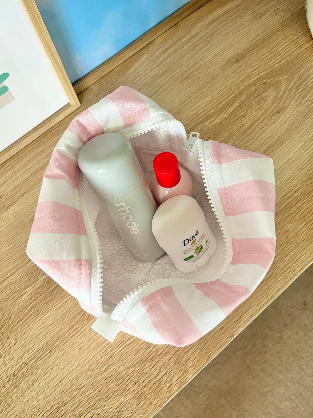 Pink and white striped makeup bag open with toiletries bottles inside.