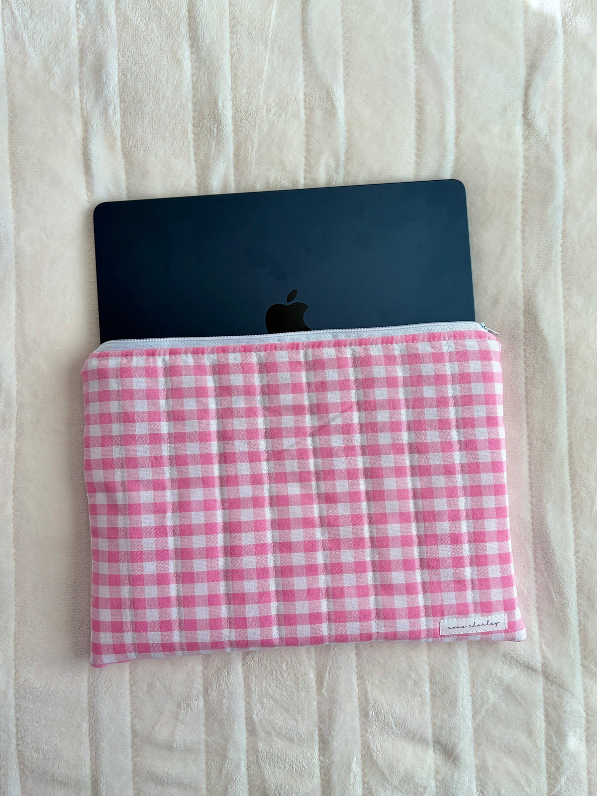 Pink gingham laptop sleeve holding a dark tablet or laptop, closed top edge.