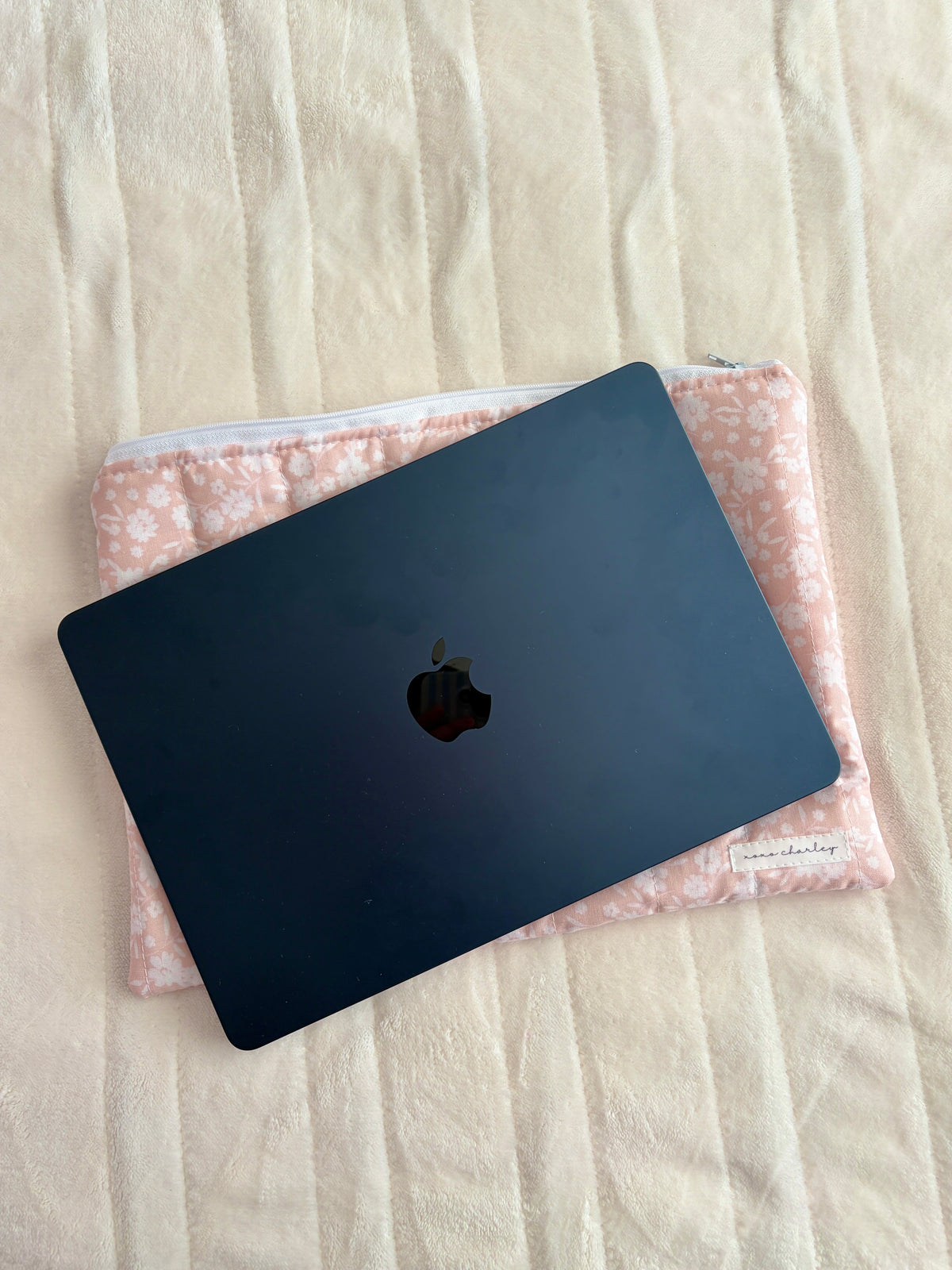 Floral laptop sleeve with light blue zipper holding a dark Apple laptop