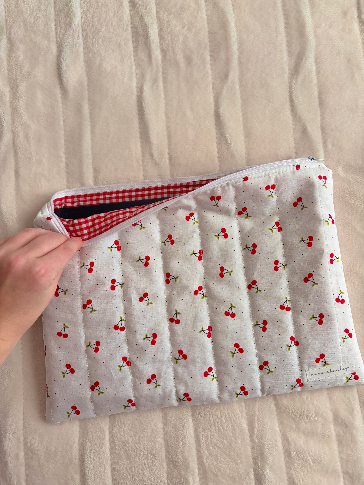 Cherry-pattern laptop and tablet sleeve with red gingham lining, hand holding the open edge