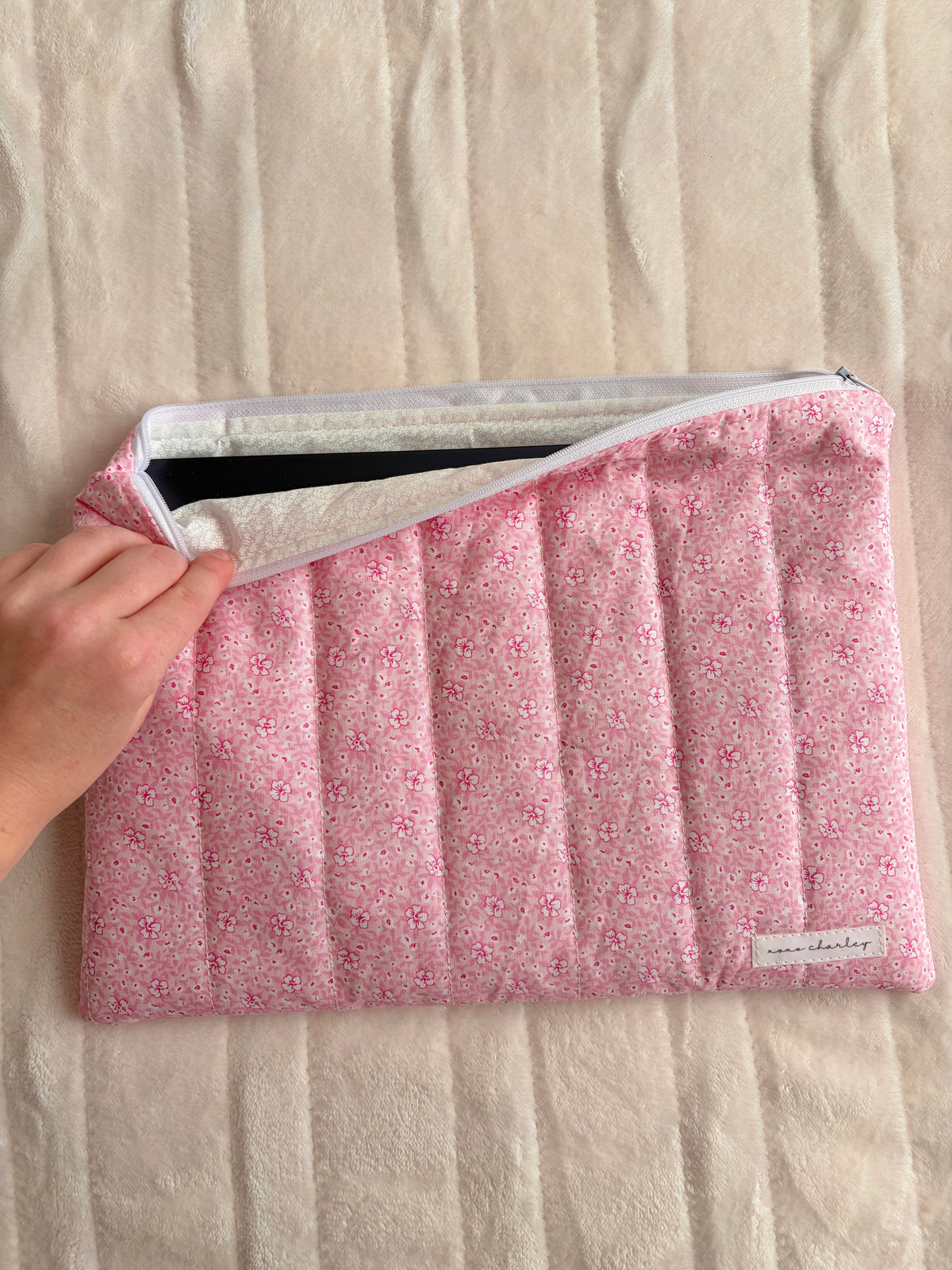 Pink floral laptop and tablet sleeve held open with gray webbing handle