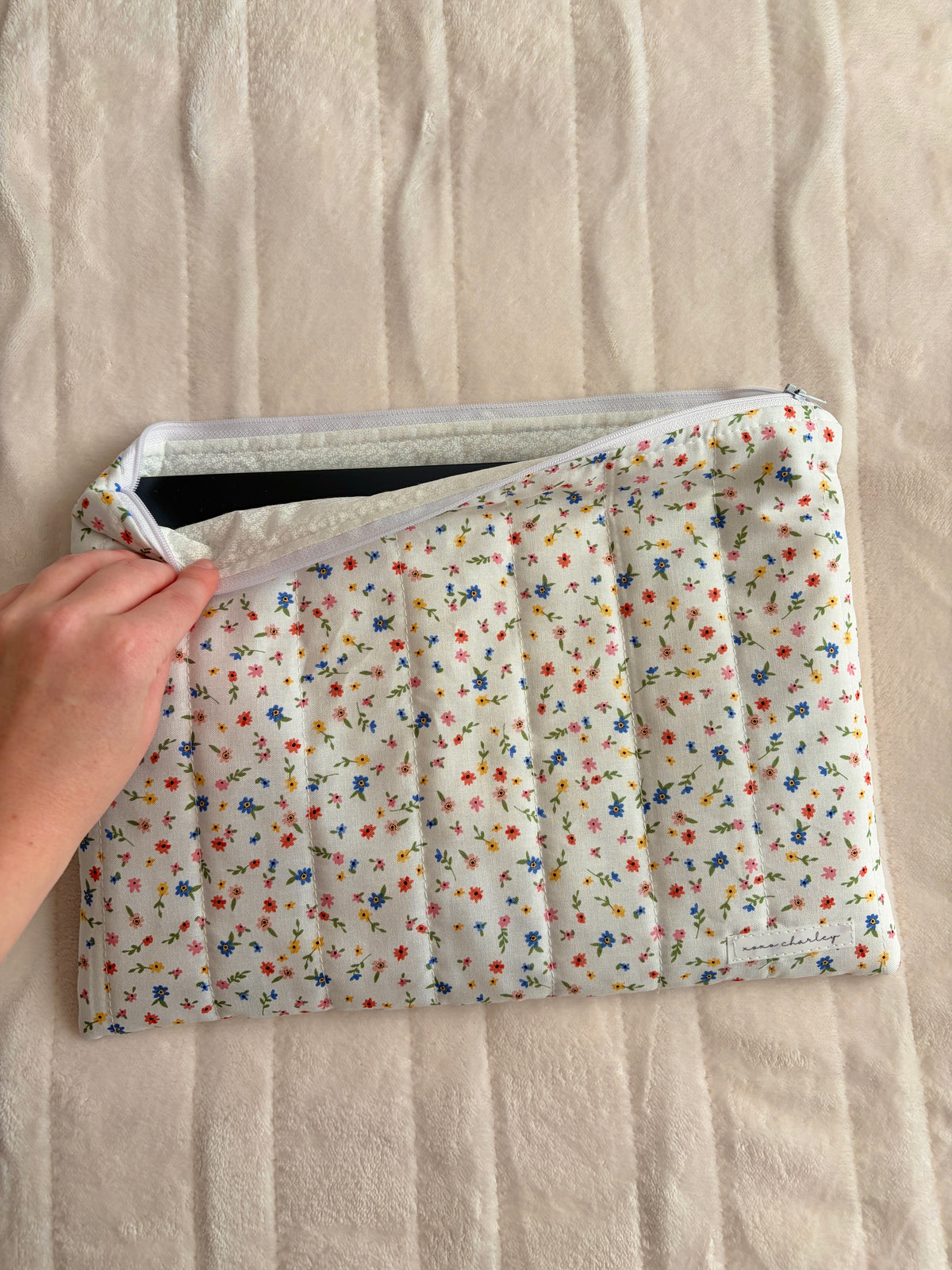 Hand holding open floral laptop & tablet sleeve with padded interior and zipper opening.