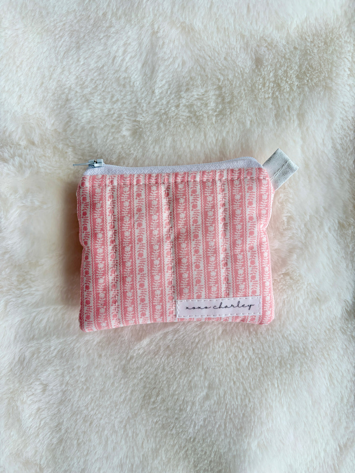 Small pink pouch with text pattern on a white fur background
