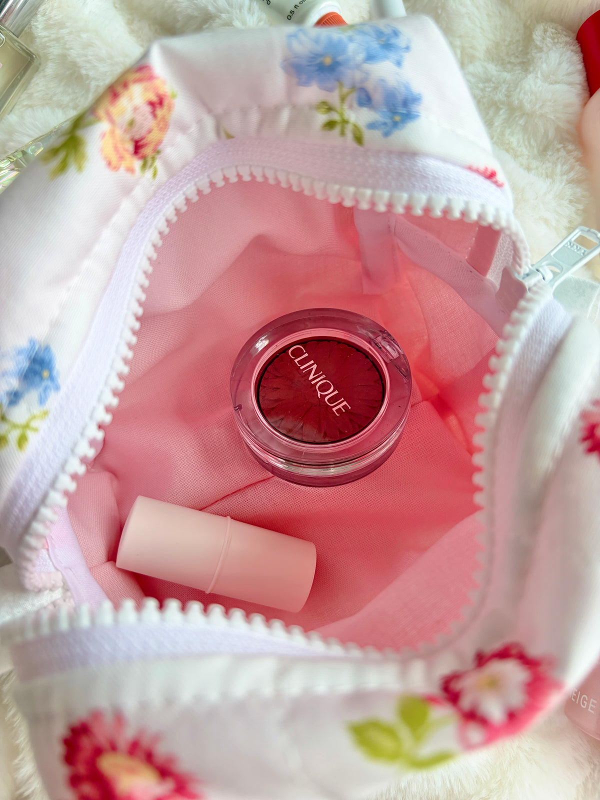 Martha Pink mini makeup bag close-up, white floral pouch with pink interior and round brand seal