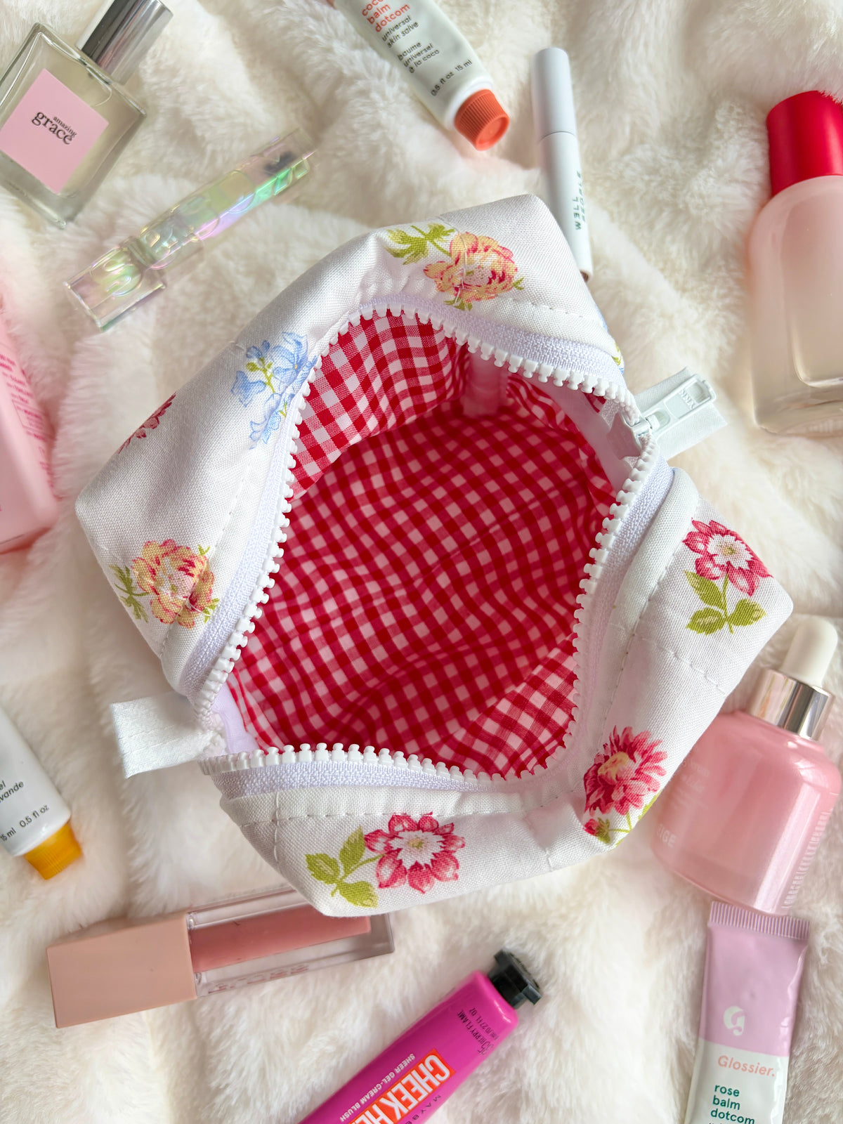 White mini makeup bag with red gingham lining, floral accents, and zipper closure