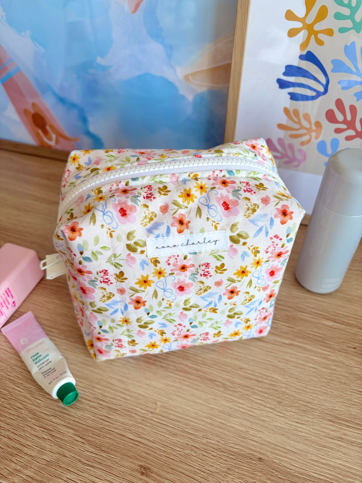Medium floral makeup bag with white zipper and multicolor flower print, front view.