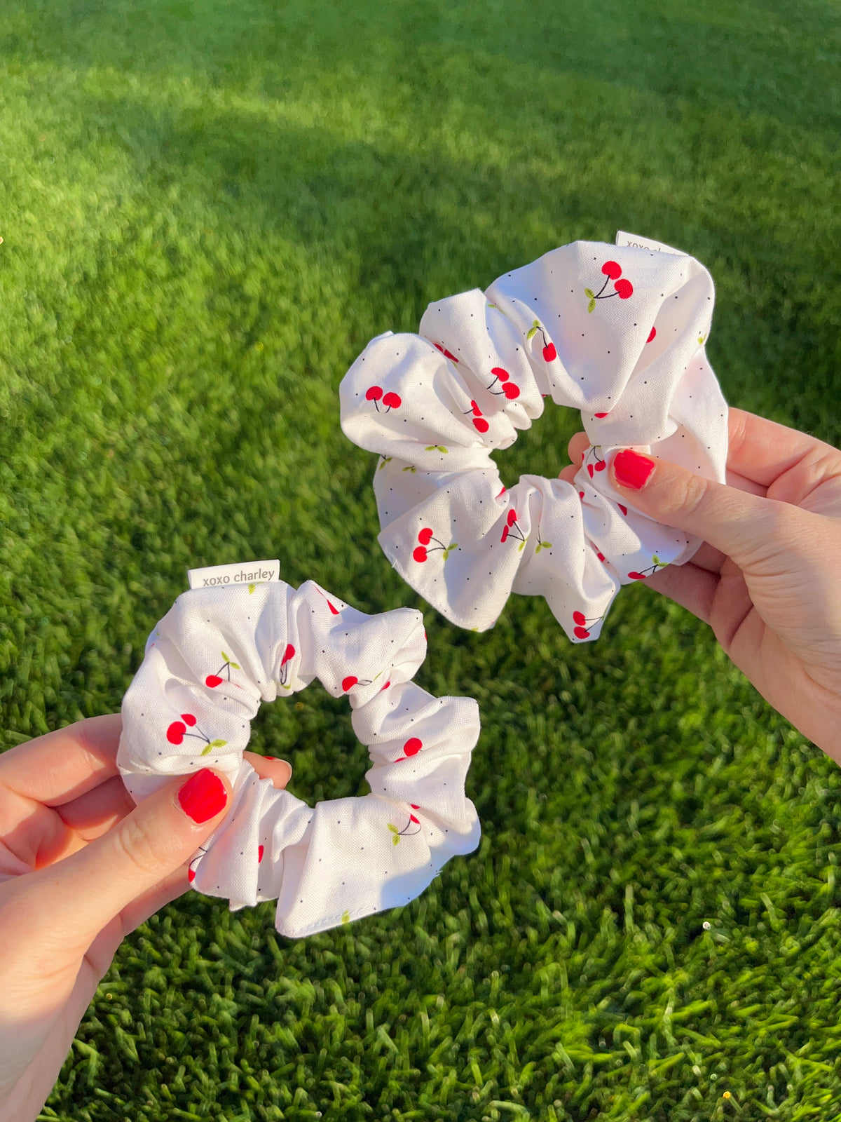 White cotton scrunchie with red cherry print, held in hands