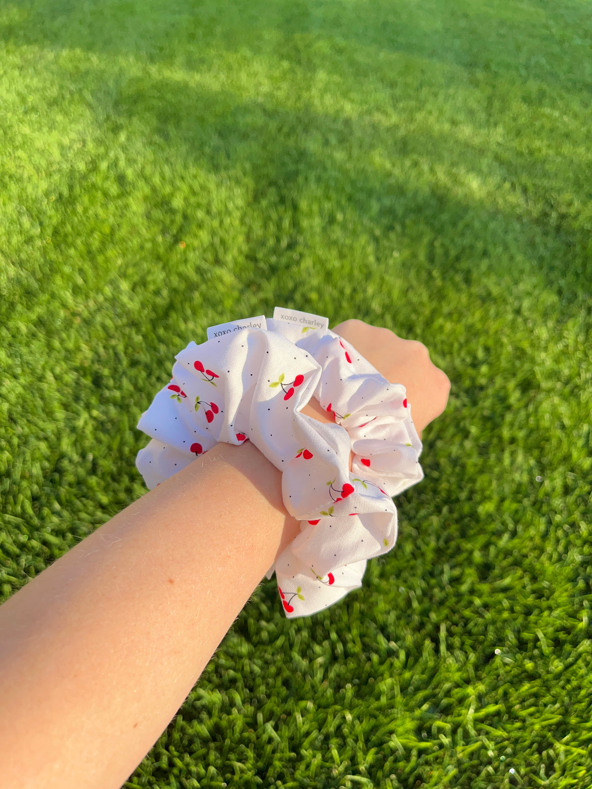 White cotton scrunchie with red cherry print, worn on wrist
