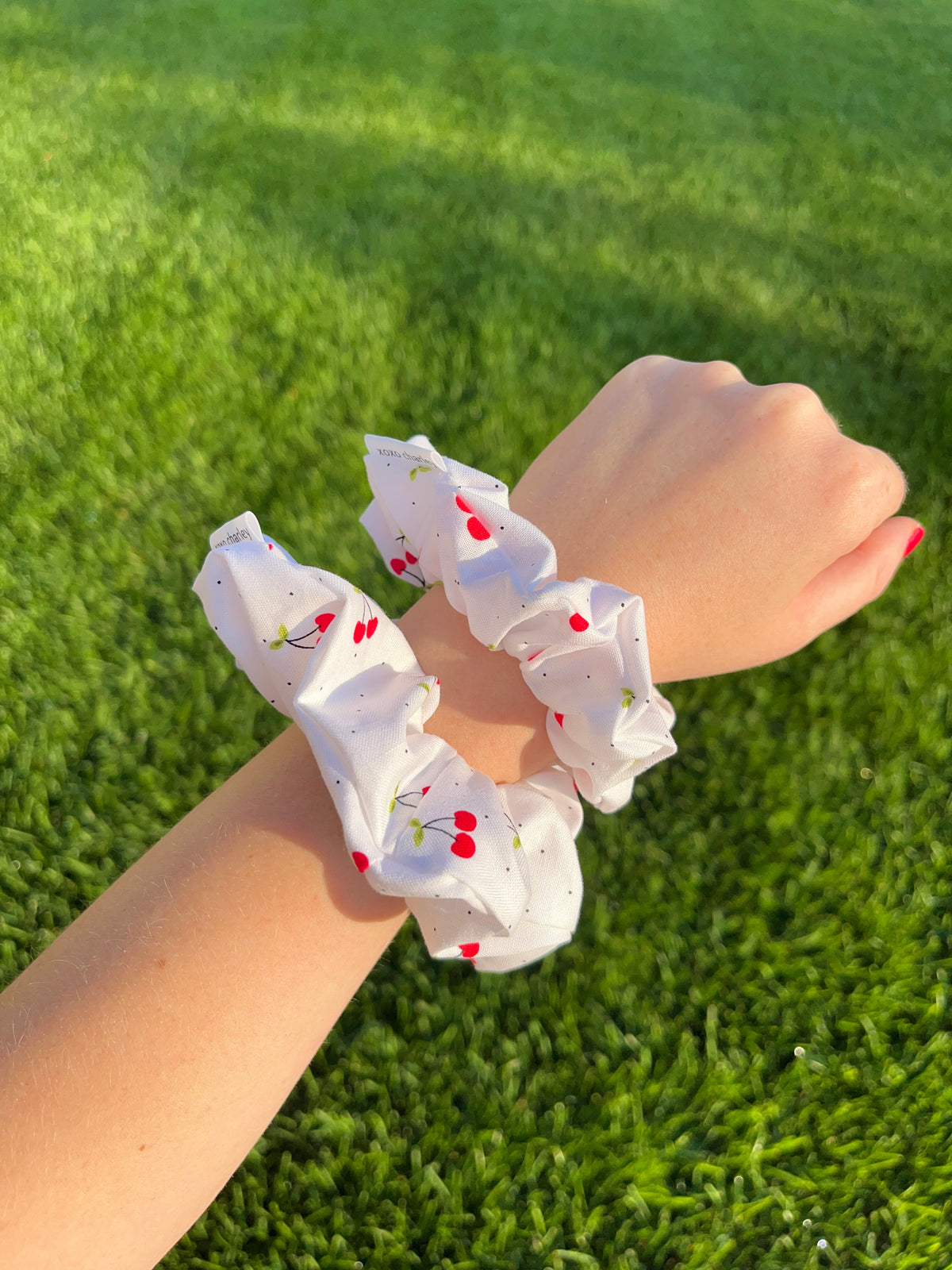 White cotton scrunchie with red cherry print, close-up on hand